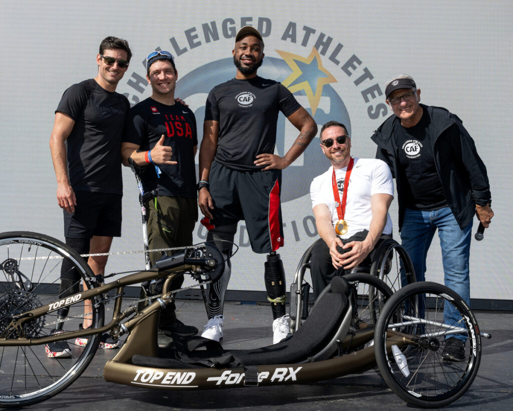 Five people posing with a racing wheelchair in front of the CAF logo.