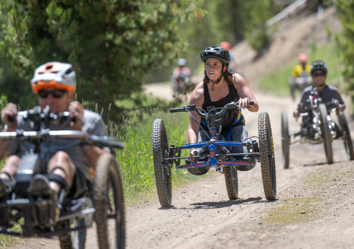 People riding adaptive mountain bikes on a forest trail.