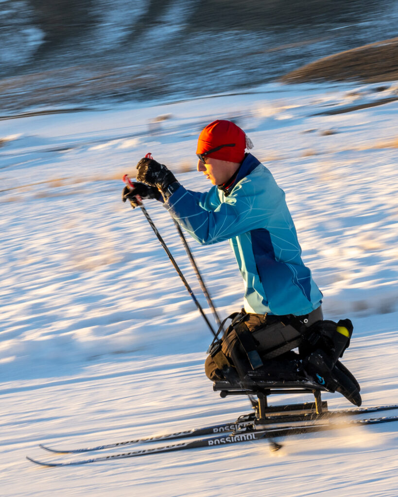 A person sit skiing on a snowy field, wearing a blue jacket and red cap.