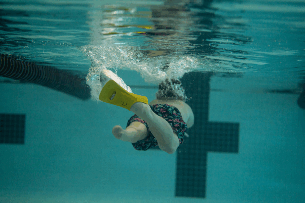 Underwater view of a young swimmer with a yellow swim fin kicking through the pool.