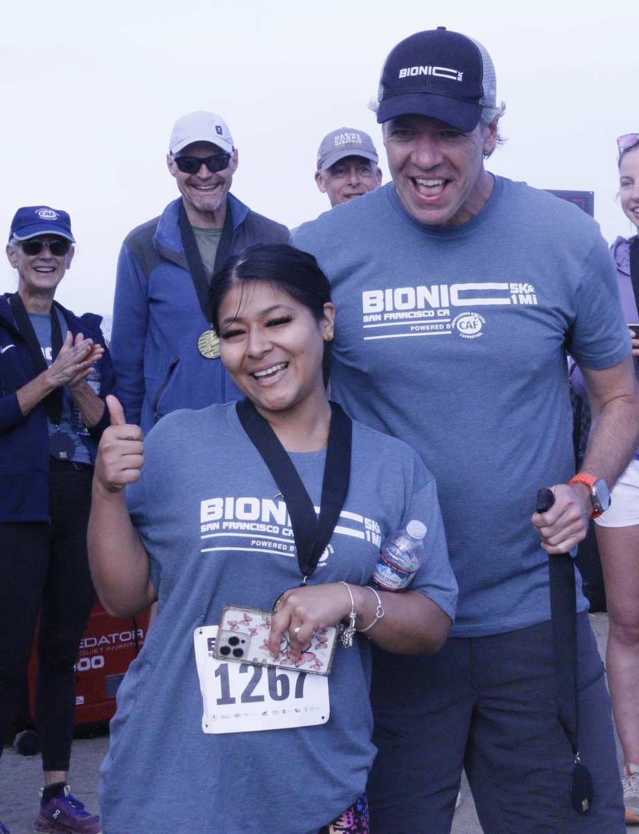 Two smiling participants wearing Bionic Mile shirts and medals celebrating at the finish line.