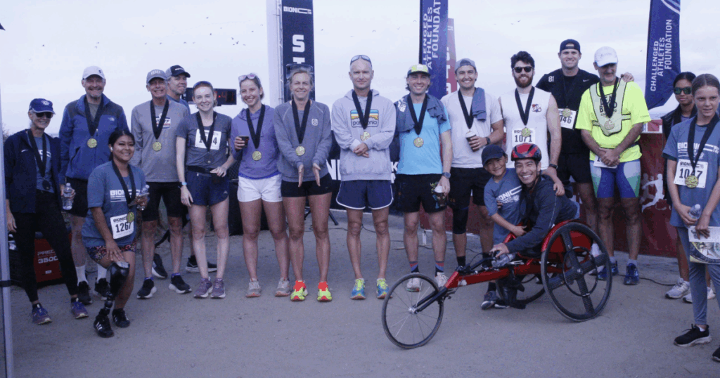Group of Bionic Mile participants wearing medals and race bibs posing together, including athletes with and without disabilities.