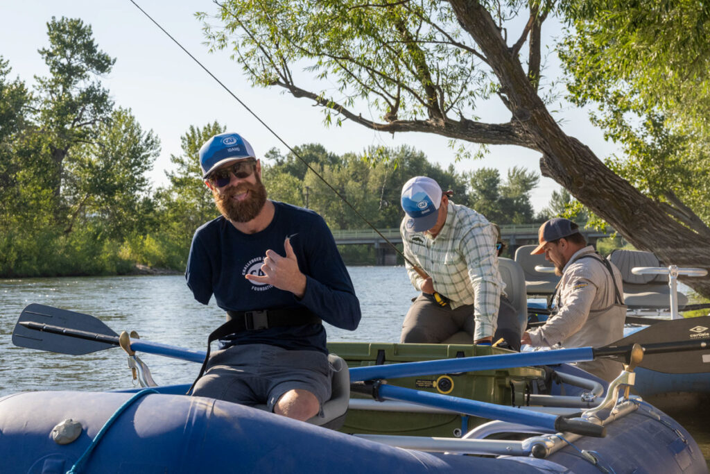 Three men on a blue inflatable raft on a river, surrounded by trees.