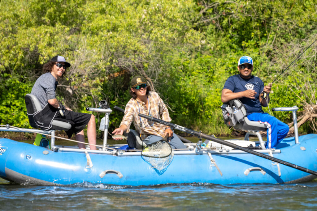 Three people fishing on a blue raft in a river.