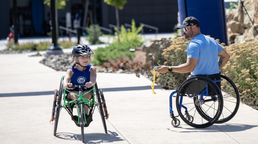 A CAF mentor in a wheelchair talks with a young athlete during the Idaho Kids Paratriathlon Camp, highlighting mentorship and support.