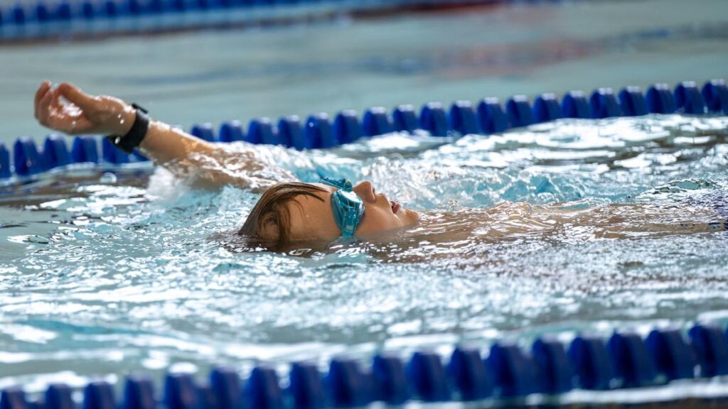A young athlete wearing goggles floats on their back in a pool during the swim portion of the Idaho Kids Paratriathlon Camp.