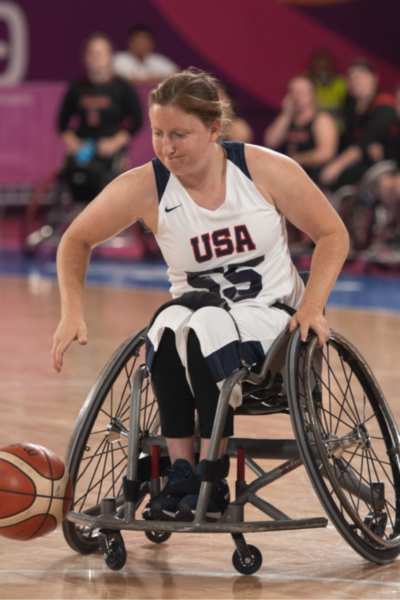 Close-up of a USA wheelchair basketball athlete controlling the ball while moving down the court during international wheelchair basketball competition.