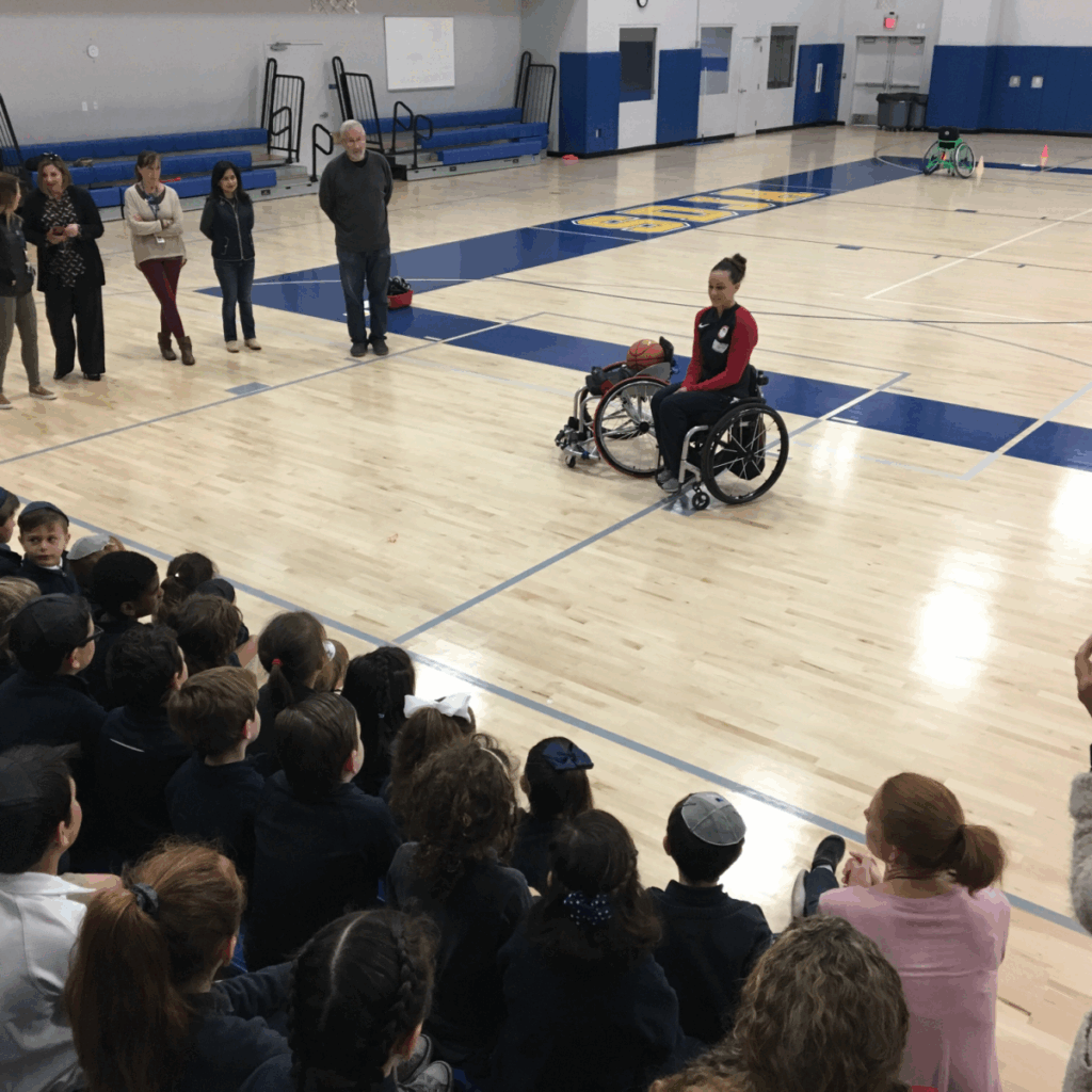 Megan Blunk speaks to an attentive group of elementary students in a school gym, sharing her story and experiences as an athlete with a physical disability.