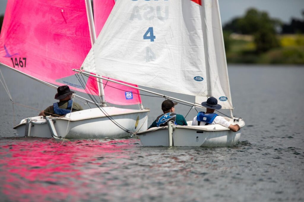 Two sailboats with pink and white sails glide across the water during an adaptive sailing activity.
