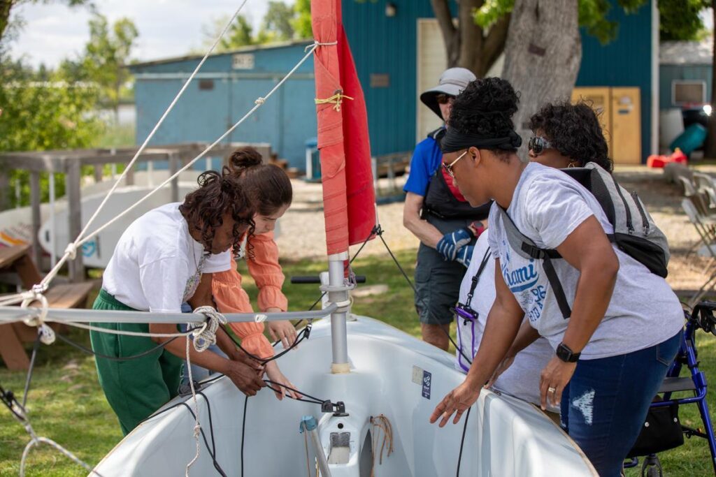 A group of participants work together to rig a sailboat on shore during an adaptive sailing program.