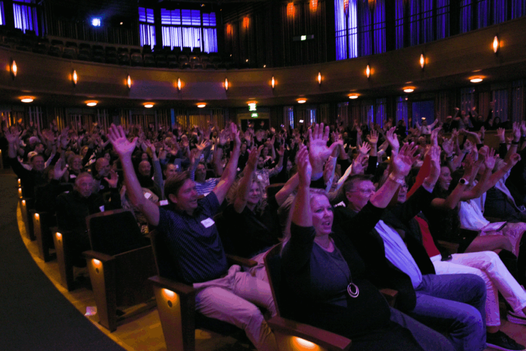Audience members at the Celebration of Abilities event raise their hands in unison inside a theater filled with energy and applause.