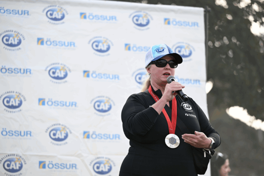 Athlete wearing a medal and CAF hat speaks into a microphone in front of a CAF and Össur step-and-repeat backdrop.