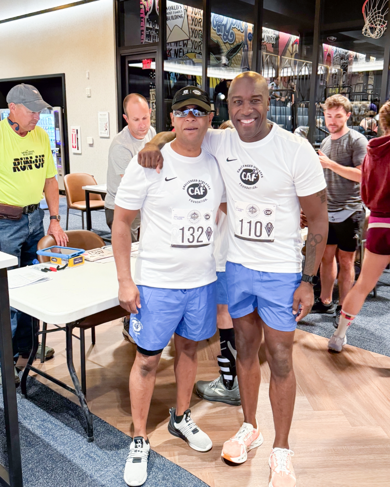 Two CAF athletes wearing race bibs pose together indoors before the Empire State Building Run-Up event.