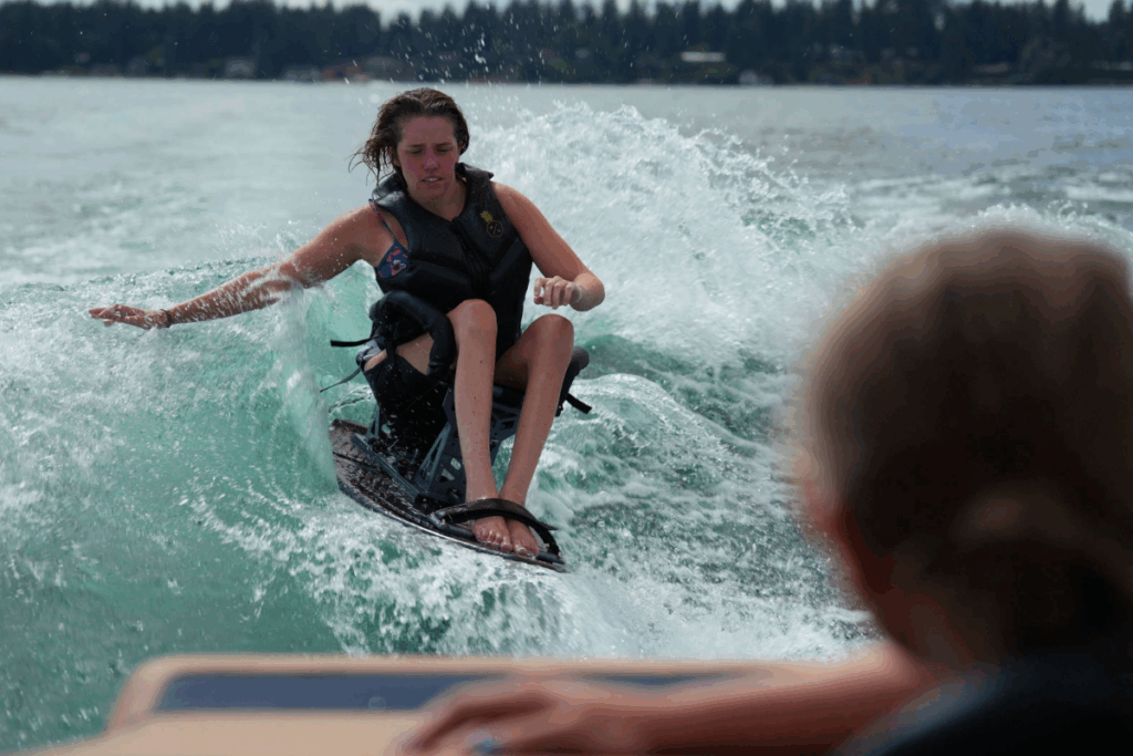 A woman wearing a life jacket carves through the water on an adaptive ski, balancing and reaching into the wave.
