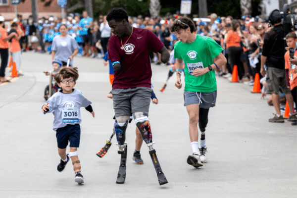 Young athletes with physical disabilities, wearing CAF shirts and prosthetic running blades, race alongside peers and supporters during the Jami Marseilles Kids Run & Roll presented by Philadelphia Insurance Companies.