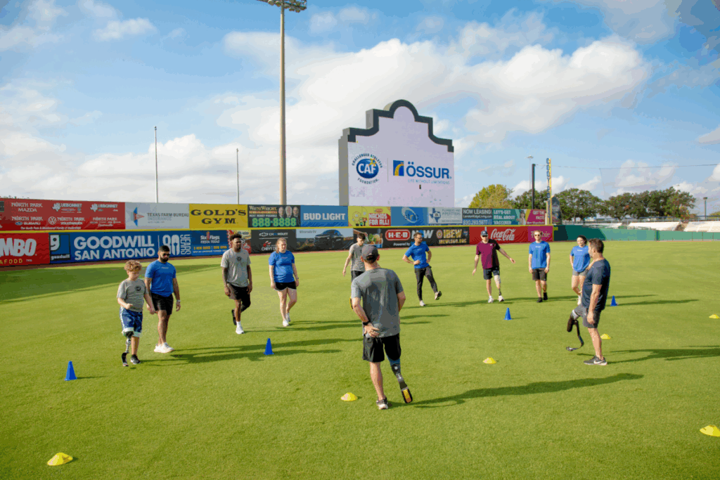 Group of participants warm up on the baseball field under a large CAF and Össur sign during a mobility clinic.