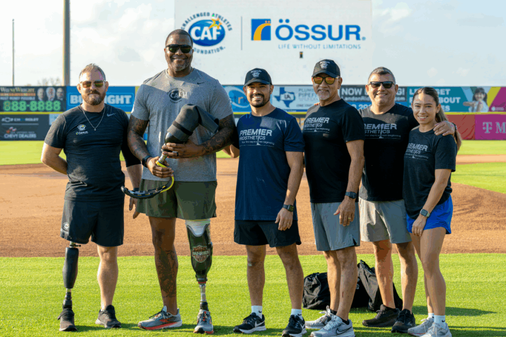 Group of athletes and coaches with prosthetic legs pose together on the field beneath a CAF and Össur sign.