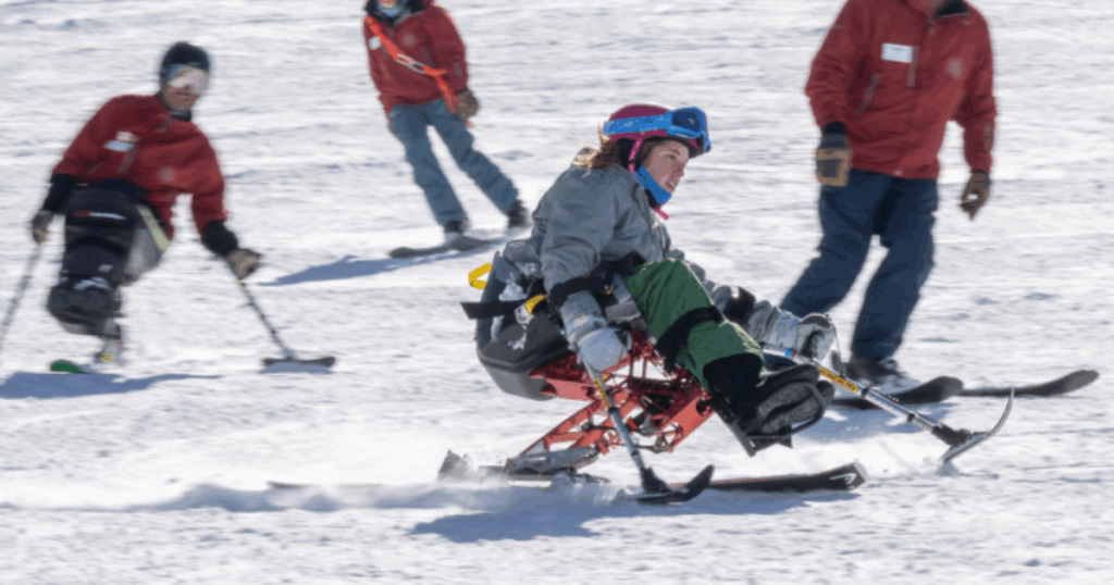 An athlete using a monoski carves through the snow during a downhill ski run, with others skiing in the background.