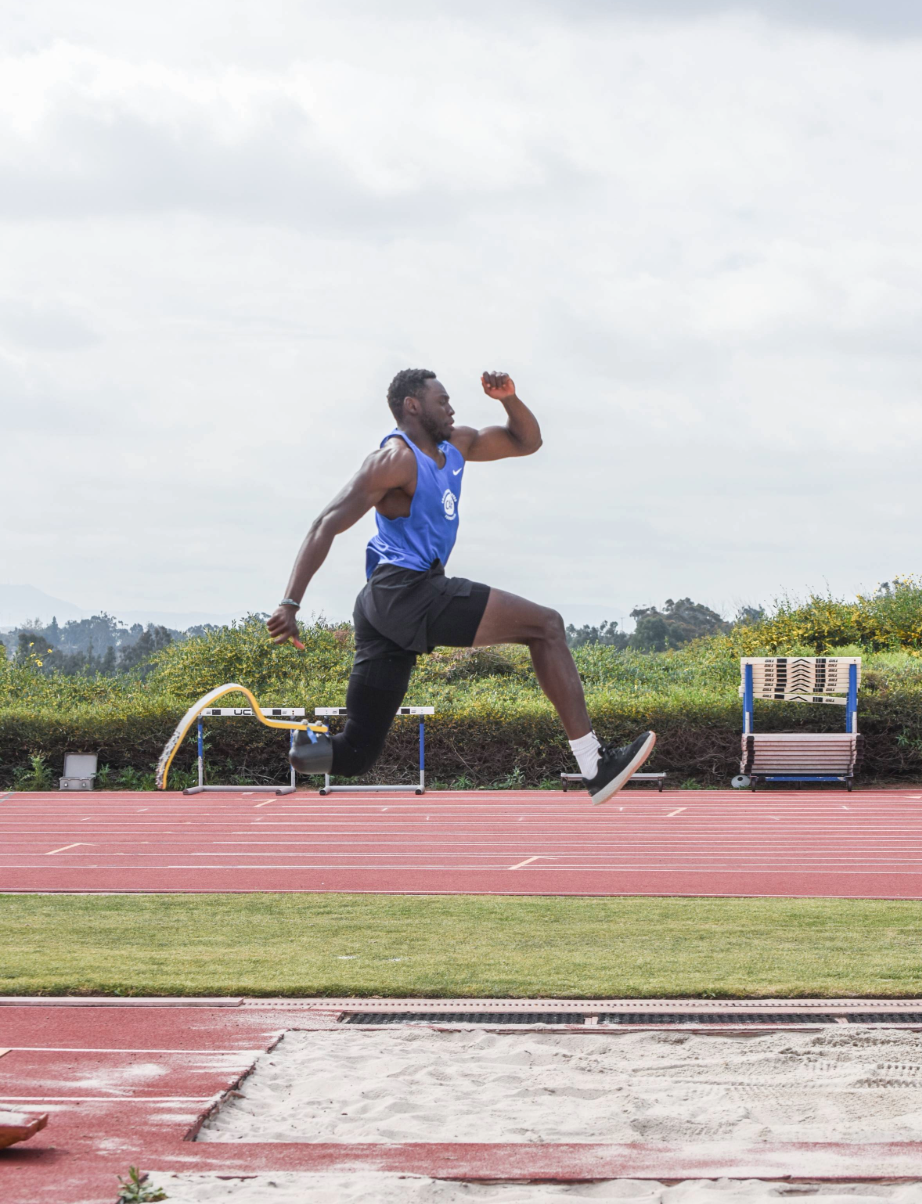 Paralympic track and field athlete with a running blade jumps into the sandpit during a long jump at an outdoor track.
