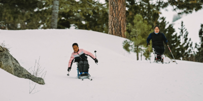 A young athlete using a monoski carves through the snow on a downhill slope, holding outriggers for balance.