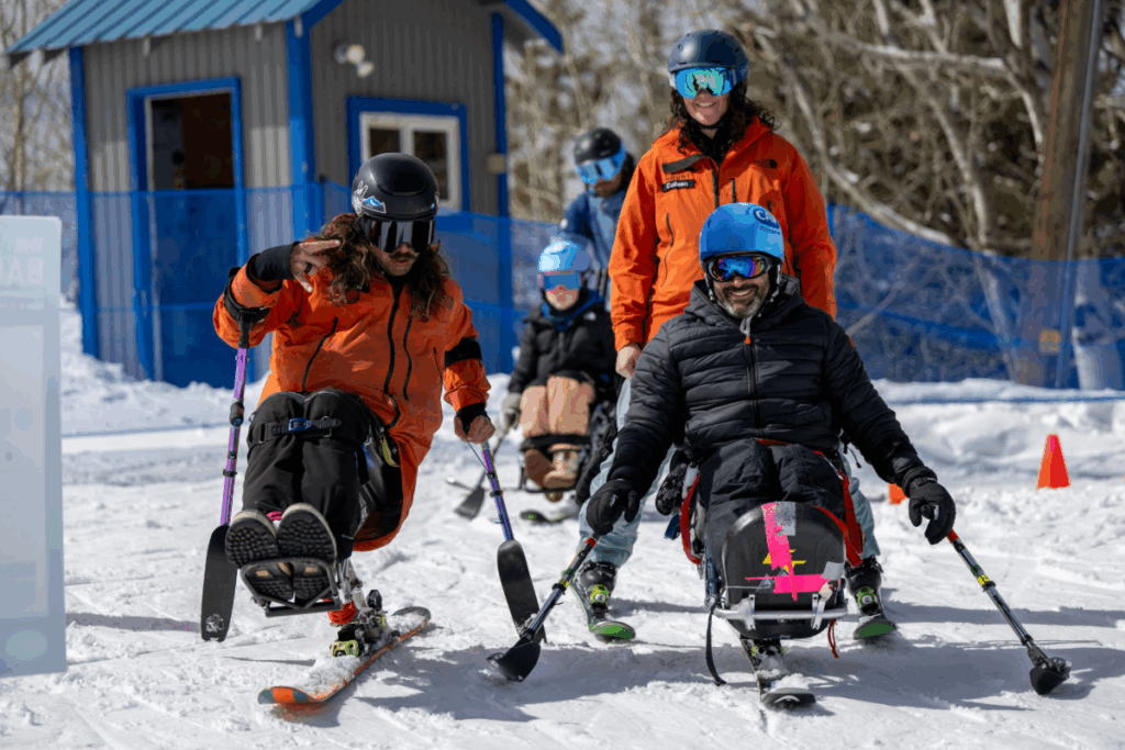 Group of athletes in sit-skis smile and train together with instructors on the mountain.