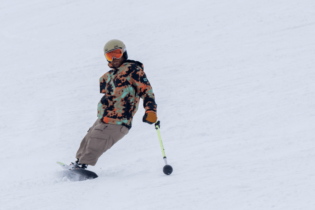 Athlete snowboards down a snowy slope using an outrig for balance during a winter basecamp.
