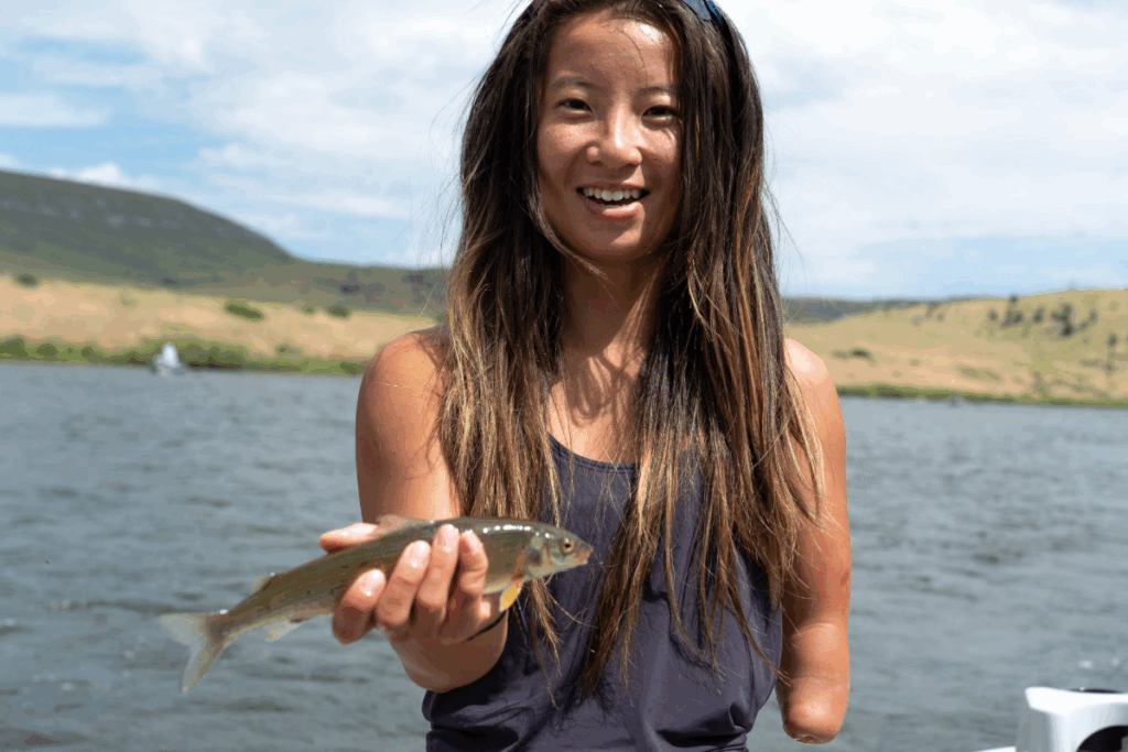 Athlete smiling while holding a small fish after a successful catch on the river.