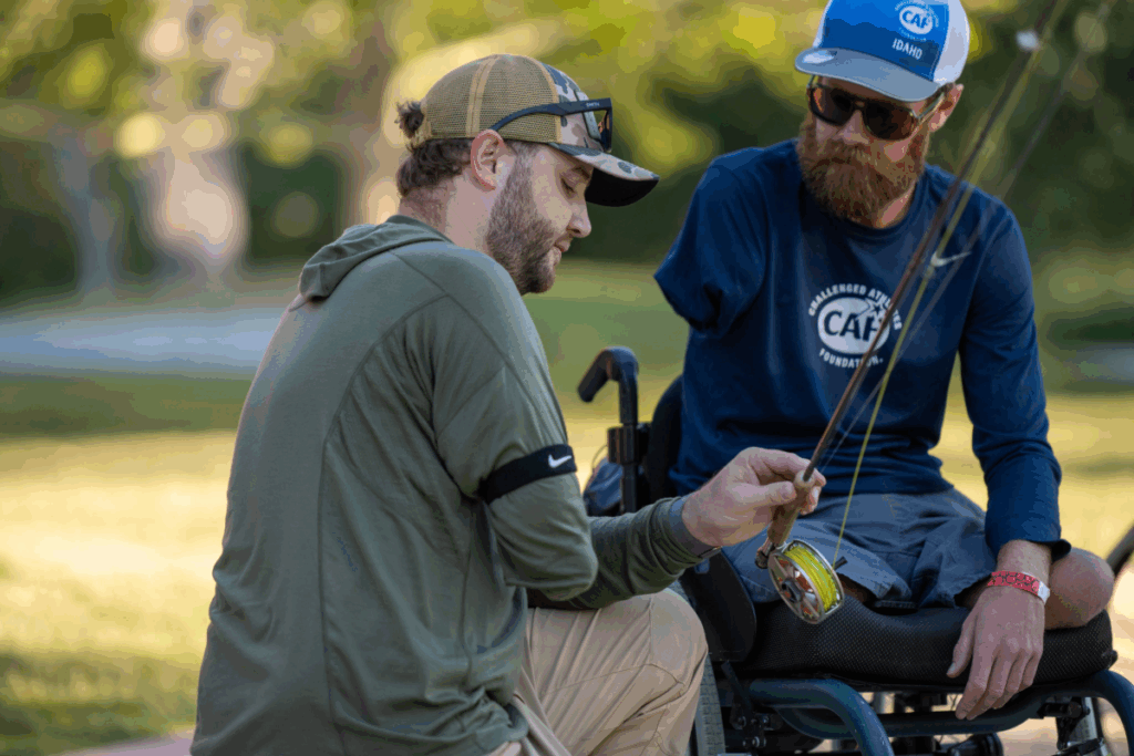 Two athletes examine a fishing reel together during a fly-fishing lesson.