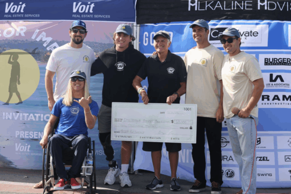 A group of six Surf for Impact participants, including one athlete using a wheelchair, pose with an oversized check for $60,000 presented to the Challenged Athletes Foundation.