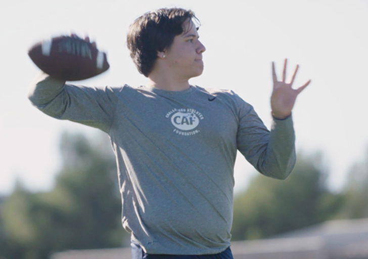Athlete with a physical disability prepares to throw a football on a practice field, focused on form and technique.
