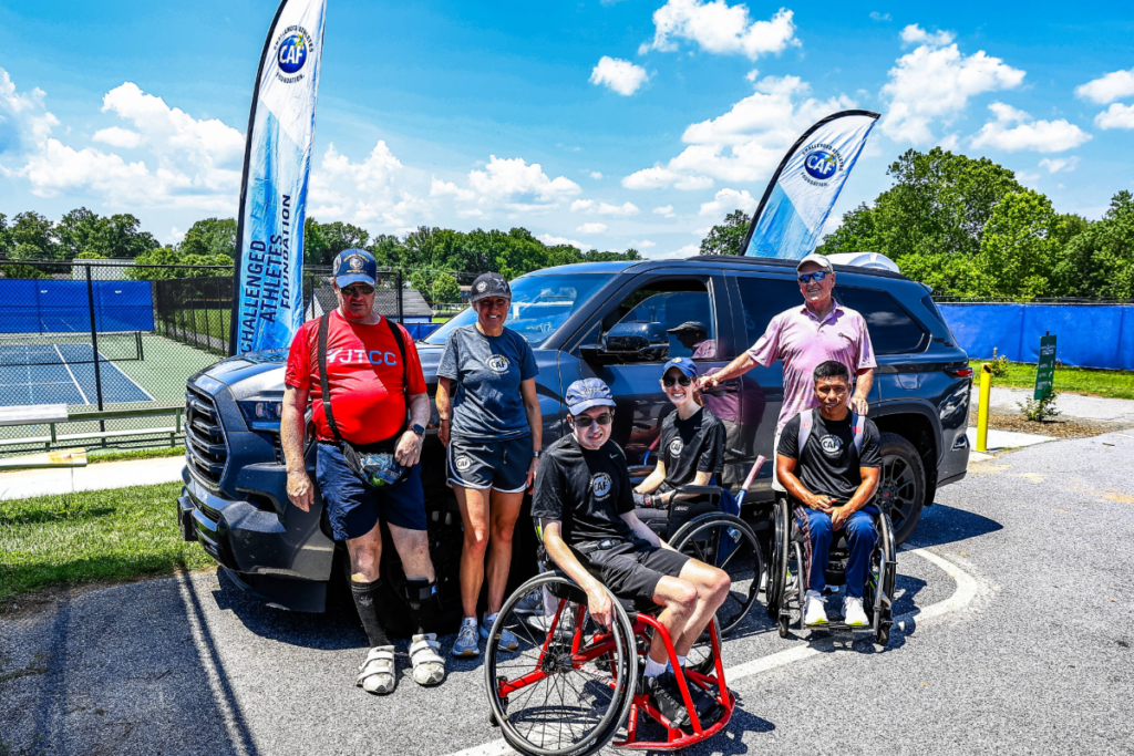 CAF athletes and volunteers stand together beside a CAF-branded vehicle at an adaptive tennis event.
