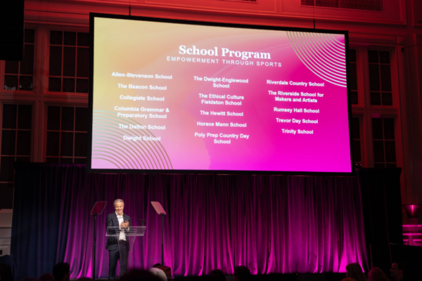 A speaker stands at a podium in front of a purple curtain as a large screen displays the CAF School Program and a list of participating schools at the Heroes, Heart & Hope Gala.