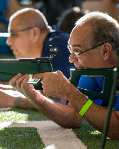 Two people lying on the grass aiming green air rifles.