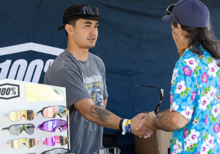 CAF partner representative shakes hands with an athlete with a physical disability at a sponsor booth displaying sports eyewear during a CAF event.