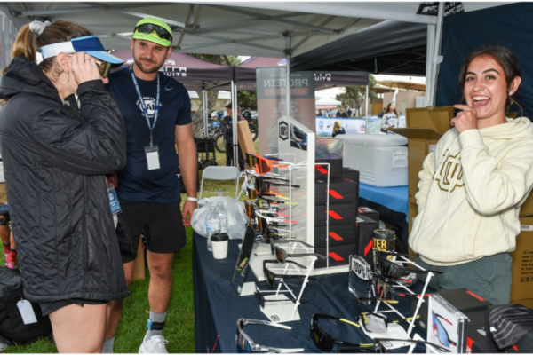 Athlete with a physical disability engages in conversation with a CAF partner representative at an outdoor event booth featuring sports eyewear.