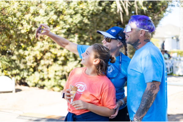 Two athletes with physical disabilities and a CAF supporter smile while taking a selfie together outdoors during a CAF community event.