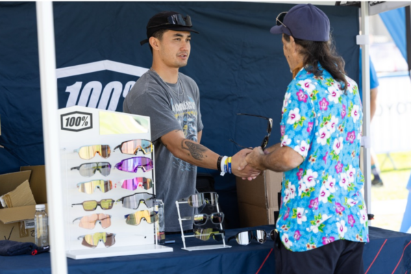 CAF partner staff assist an athlete with a physical disability as they try on sports eyewear at an outdoor CAF event booth.