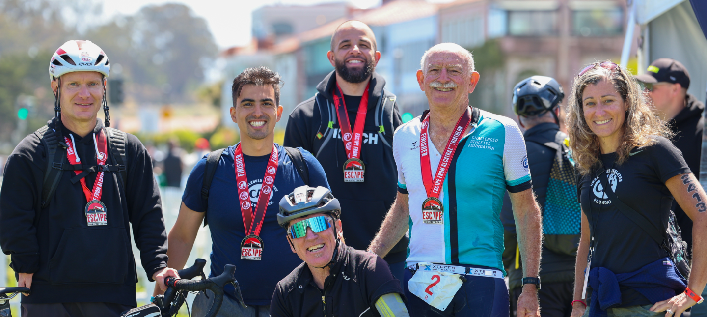 A group of athletes and supporters wearing finisher medals smile together after completing the Escape from Alcatraz Triathlon, celebrating community and achievement.