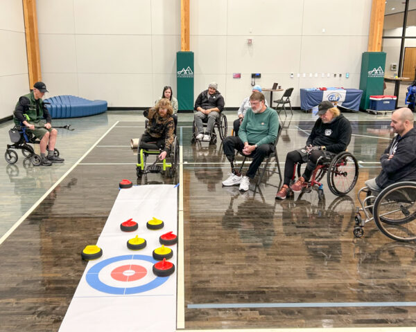 A group of individuals, some in wheelchairs, play an adaptive curling game indoors.