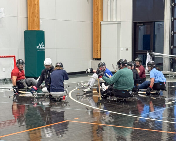A group of people playing sled hockey indoors on a glossy court.