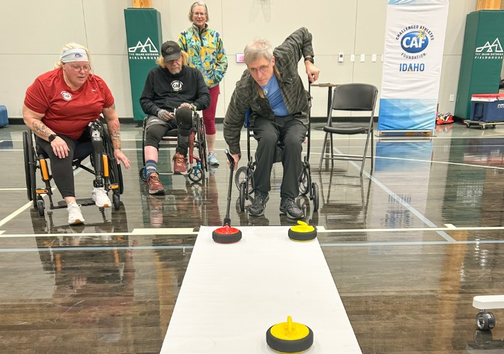 Three individuals in wheelchairs playing a curling game in a gymnasium.