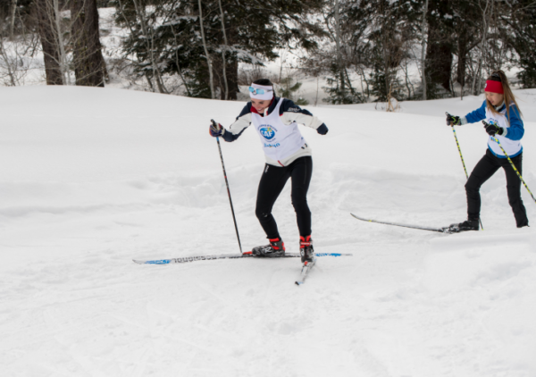Paralympian Dani Aravich cross-country skis on a snowy trail during a Nordic training session, wearing a CAF Idaho training bib.