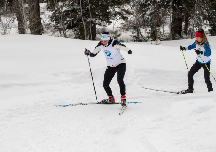 Paralympian Dani Aravich cross-country skis on a snowy trail during a Nordic training session, wearing a CAF Idaho training bib.