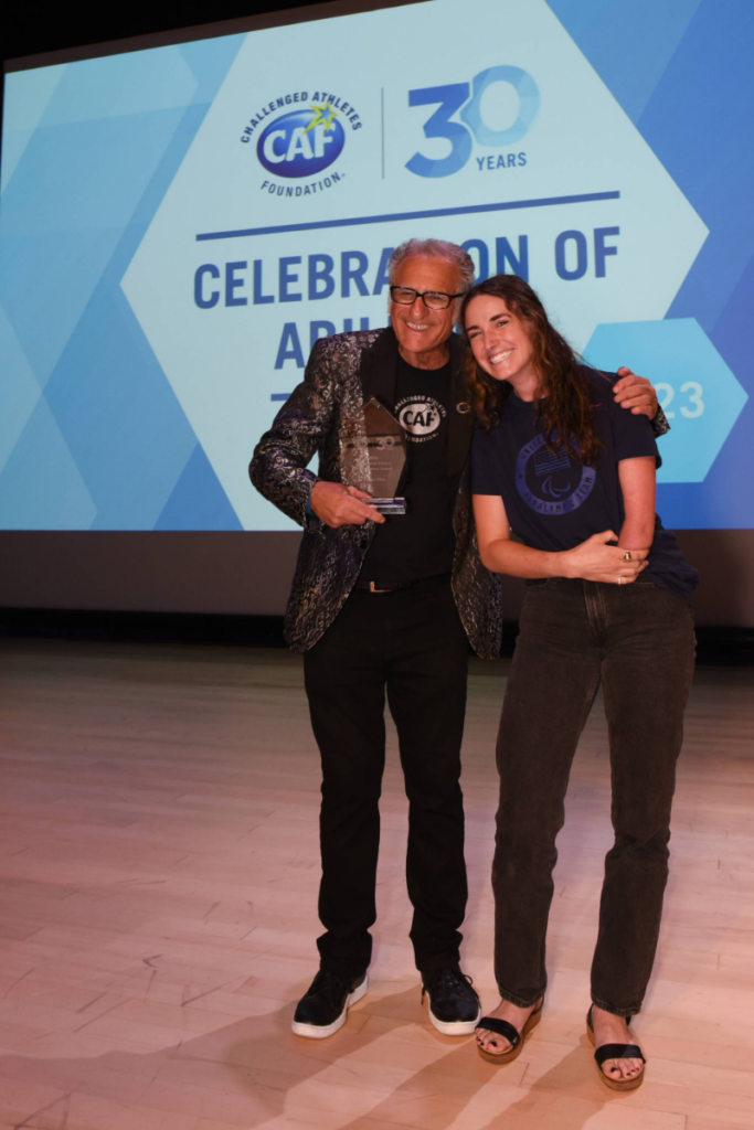 Dani Aravich smiles beside a presenter while holding an award at a CAF Celebration of Abilities event.