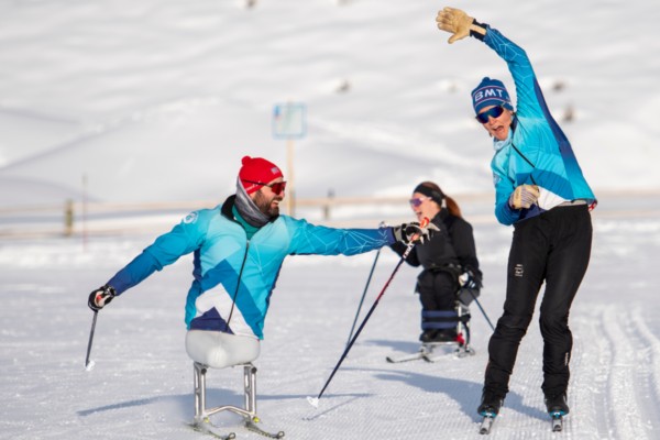 Athletes with physical disabilities participating in cross-country skiing, including a sit-ski user and standing skiers, moving together across a snowy course.