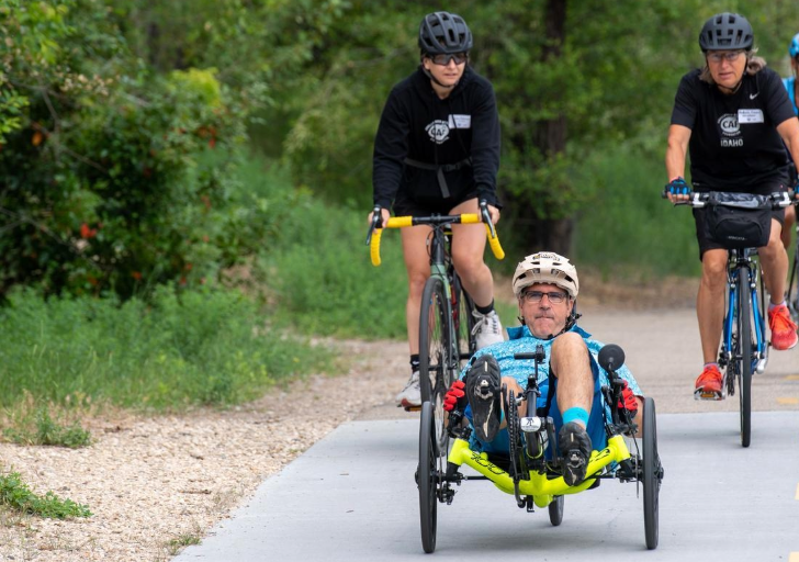 Inclusive cycling group trains together on a scenic path, with a handcycle rider at the front and cyclists following.