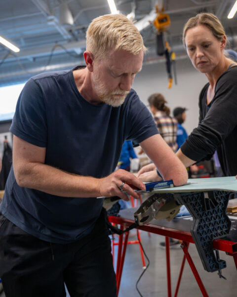 Two individuals working on a project at a red table in a workshop setting.