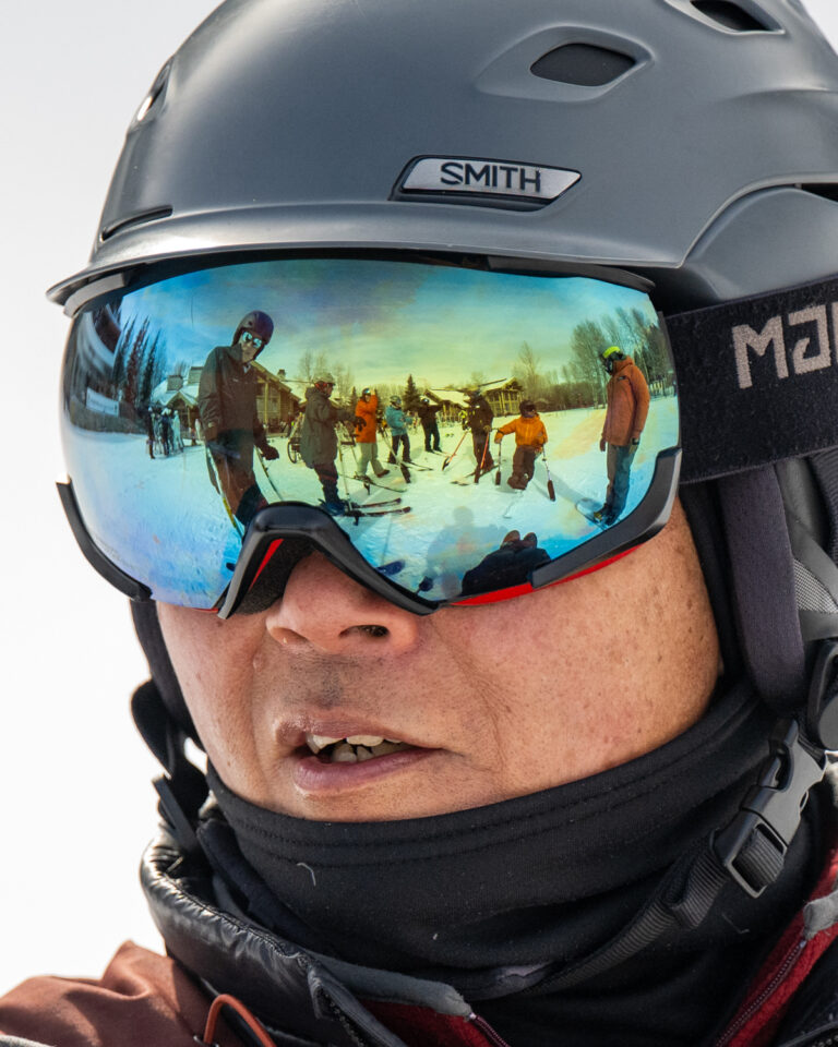 Close-up of a person wearing a ski helmet and reflective goggles showing a winter scene.