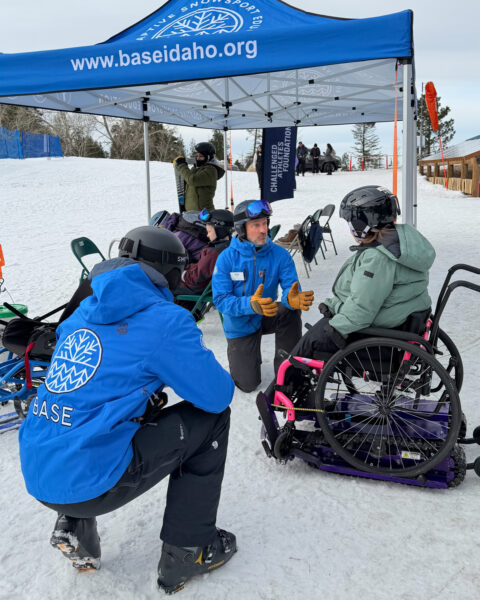 People in snow gear interacting near a blue tent marked with "BASE Idaho."