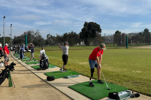 Group of athletes with physical disabilities participate in a CAF adaptive golf clinic, practicing swings together on a sunny driving range in San Diego.